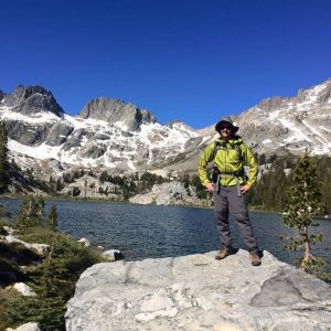 Richard Huskey stands on a rock in front of an alpine lake in the mountians
